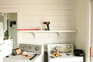 farmhouse laundry room shiplap wall with open shelves and washer and dryer during remodel