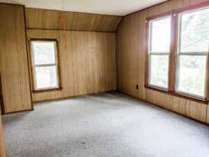 farmhouse upstairs bedroom with floor to ceiling wood panel walls multiple windows and carpeted floors