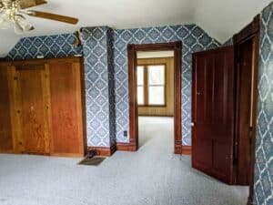 old farmhouse bedroom with blue wallpaper and original woodwork prior to renovation