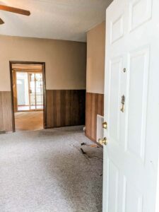 looking through farmhouse front door into front living room with carpet and wood panel walls