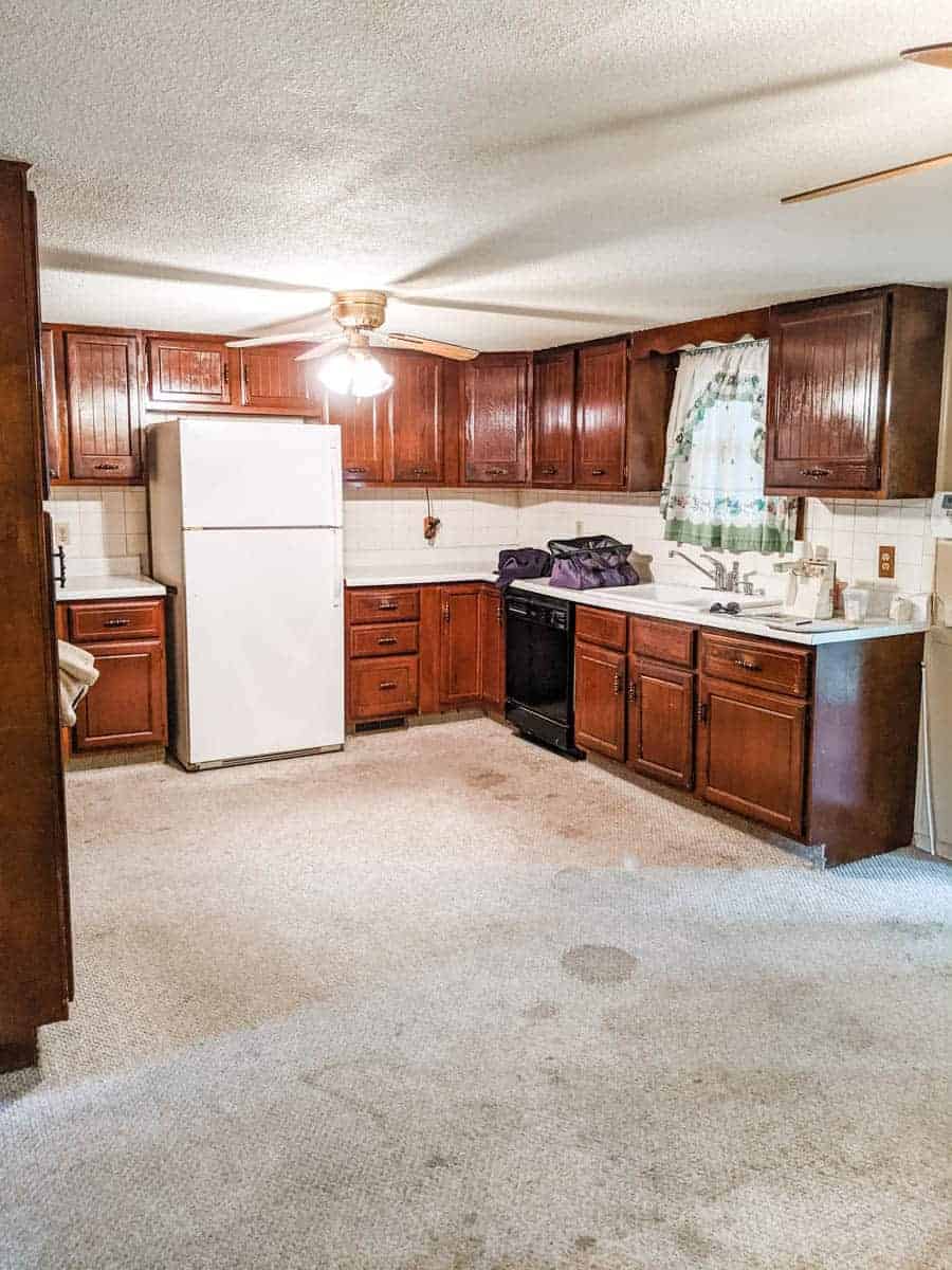 farmhouse kitchen prior to remodel with carpeted floors dark cabinets and mismatched appliances