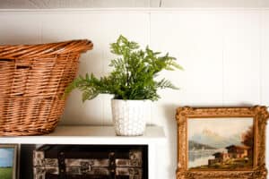 faux plant on shelf next to woven basket and vintage painting