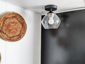 mid century style gold and black ceiling light against black cabinet and white walls with hanging basket decorations