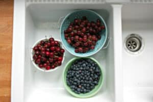 bowls filled with fresh grapes cherries and blueberries sitting in white farmhouse kitchen sink