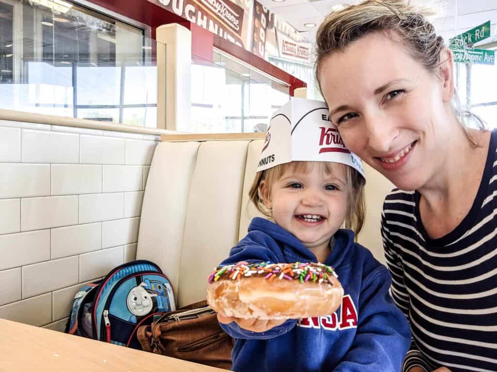 a mother and her little girl sharing a krispy kreme donut while out garage saleing