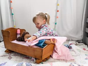 little girl playing with doll and cradle