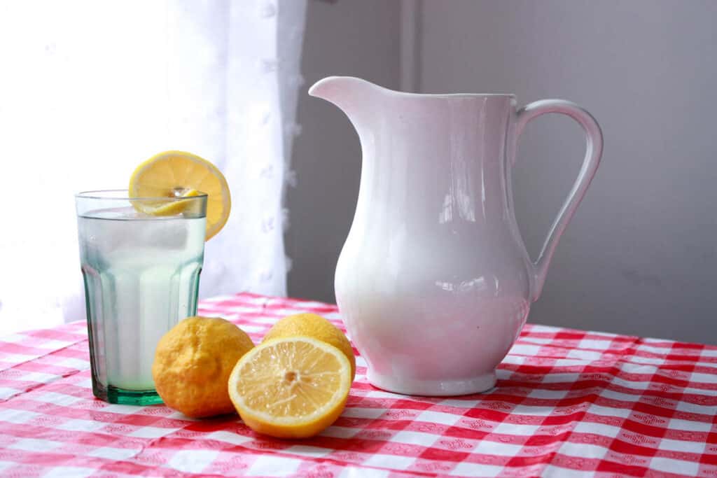 red and white checkered tablecloth with white pitcher and glass of water with lemons