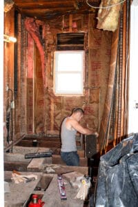 man removing walls and floor boards of craftsman bungalow bathroom to remodel it