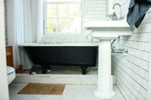 looking into a bungalow bathroom with white tile black and white clawfoot tub white pedestal sink and white shower curtain