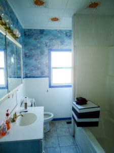 bungalow bathroom prior to remodel with blue fish wallpaper painted ceiling gold fixtures and shower tub combo