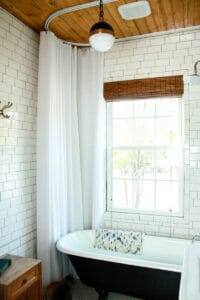 white tiled bungalow bathroom with black and white clawfoot tub natural wood ceilings and white shower curtain