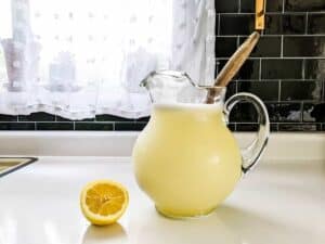 glass pitcher of homemade sugar free no squeeze lemonade and half a lemon sitting on kitchen counter