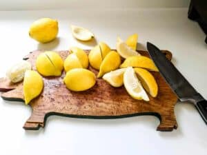 sliced lemon wedges sitting on top of wooden pig shaped cutting board with knife on kitchen counter