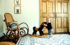mid century nursery after remodel with little boy holding onto rocking horse standing on plush rug