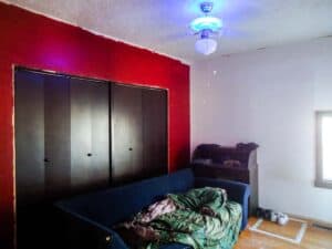bungalow bedroom before remodel with red and white walls dark brown folding closet doors and couch