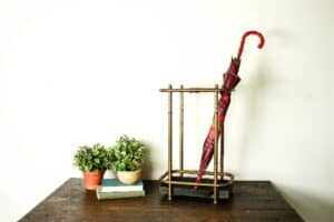 vintage umbrella holder with red umbrella staged with books and potted plants on a wooden table