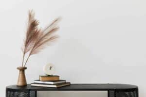 mid century modern console table with stack of books clock and dried grasses in vase
