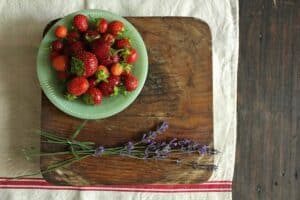 jadeite bowl full of strawberries on top of wooden cutting board adorned with stalks of lavender