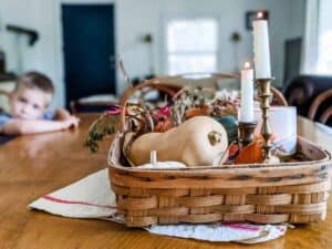 wooden basket filled with butternut squash candlesticks and fall foliage sitting on dining room table with linen towel