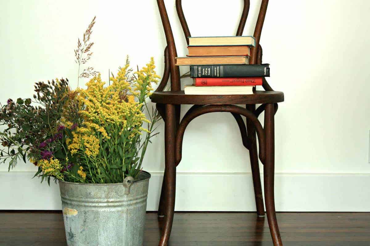 fall decor of galvanized bucket with wild flowers and a brown wooden chair with a stack of books on it