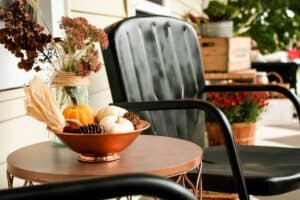 bungalow porch with fall decor of mums pumpkins dried flowers a metal chair and table and wood crate
