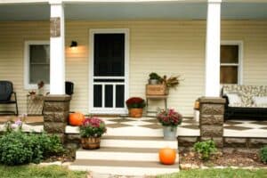 front view of bungalow porch with checkered floor mums pumpkins outdoor furniture and cream siding