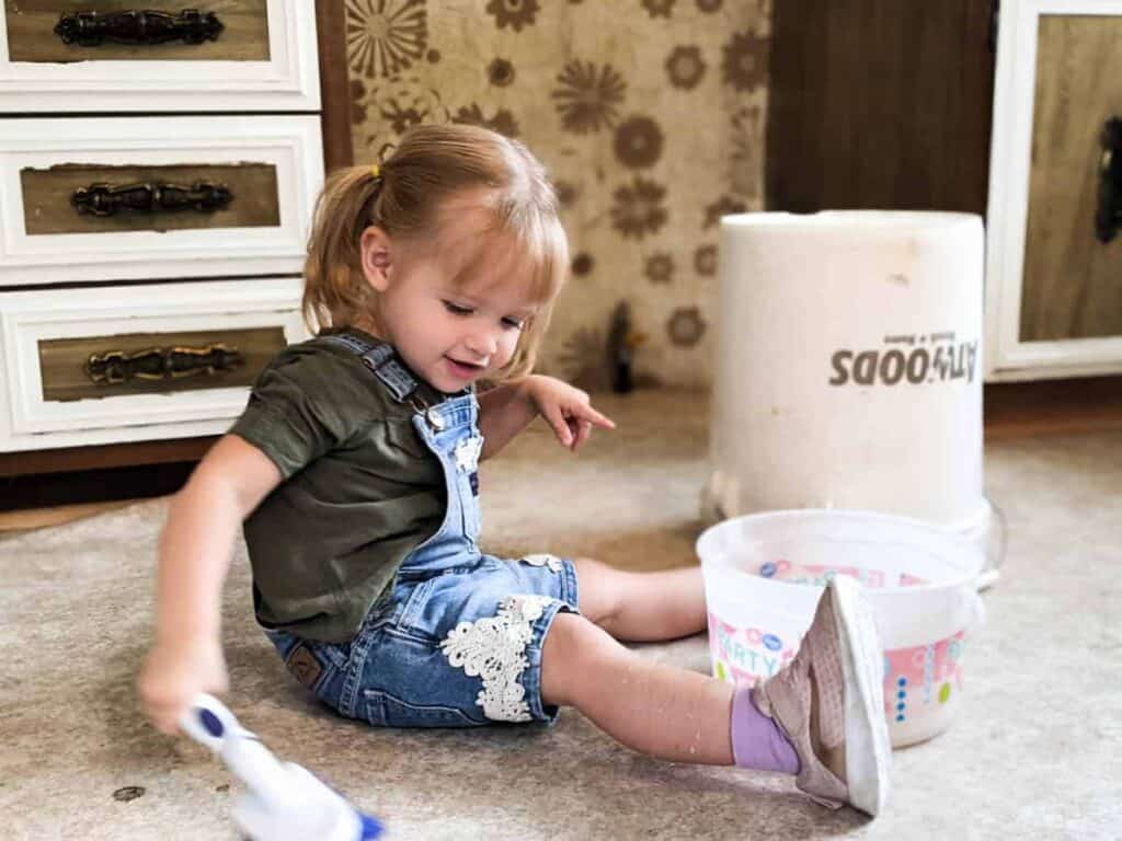 little girl scrubbing mobile home kitchen floor with hand held brush during renovation