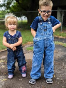 little girl and little boy standing outside in overalls and navy blue short sleeved shirts