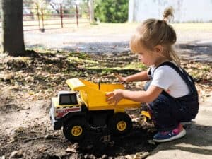 little girl plays with tonka dump truck outside