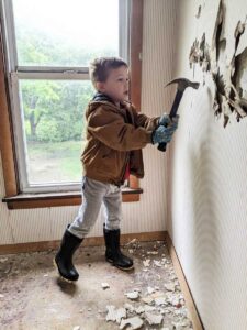 little boy helps to knock out old sheet rock from 1900s farmhouse walls with hammer