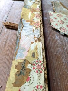 samples of multiple antique farmhouse wallpapers adhered to board found during renovation