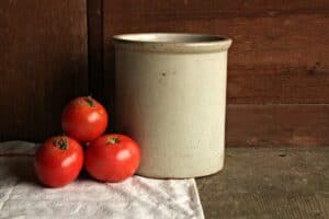authentic vintage farmhouse stone crock with red tomatoes and linen towel against wooden wall