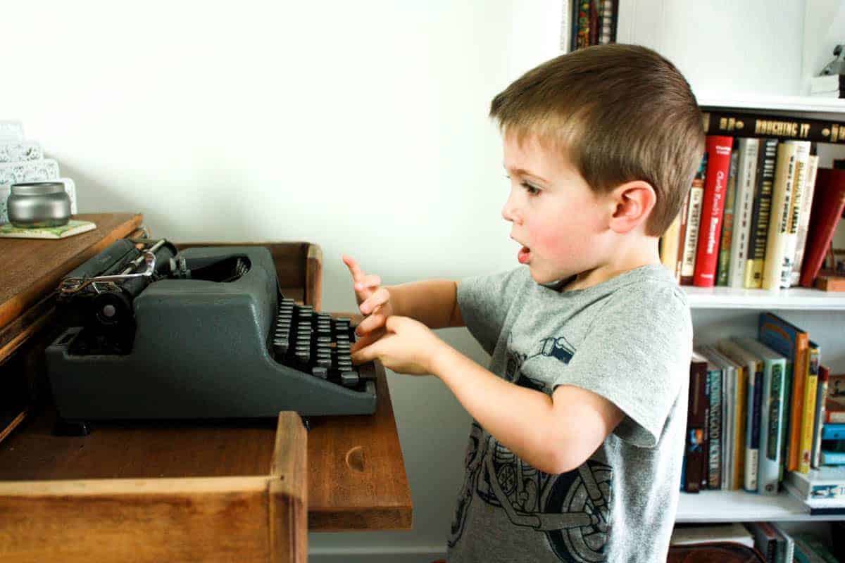 little boy playing with authentic vintage typewriter while sitting at wooden desk