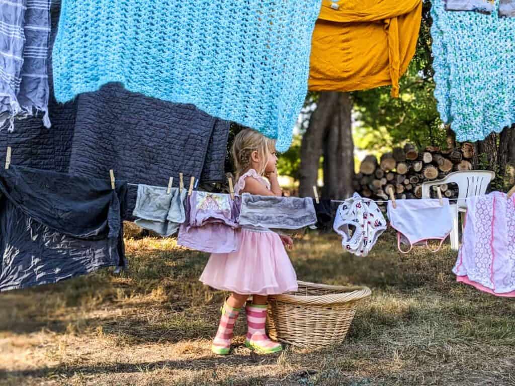 little girl playing outside amongst clothing items drying on clothes line