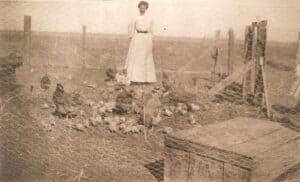 sepia toned picture of grandma johnson standing amidst chickens in a chicken coop