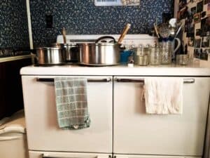vintage white kitchen stove covered in large cooking pans and empty glass canning jars