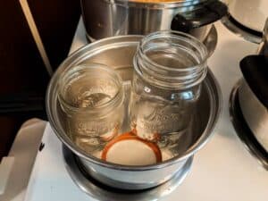 small saucepan filled with water and canning jars on stovetop during canning process of peach butter