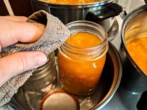 wiping down canning jar filled with peach butter prior to sealing with lid