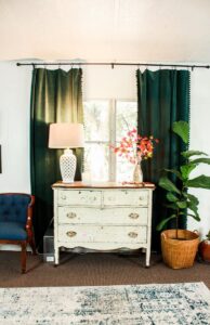 mobile home living room with chippy farmhouse dresser green velvet curtains and blue side chair