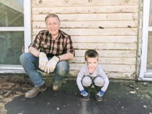 grandfather and grandson kneeling outside of old farmhouse during renovation process