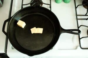 cast iron skillet with butter slices sitting on top of gas stove top