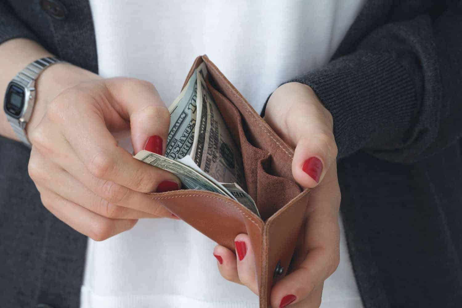 woman holding an opened leather wallet containing cash