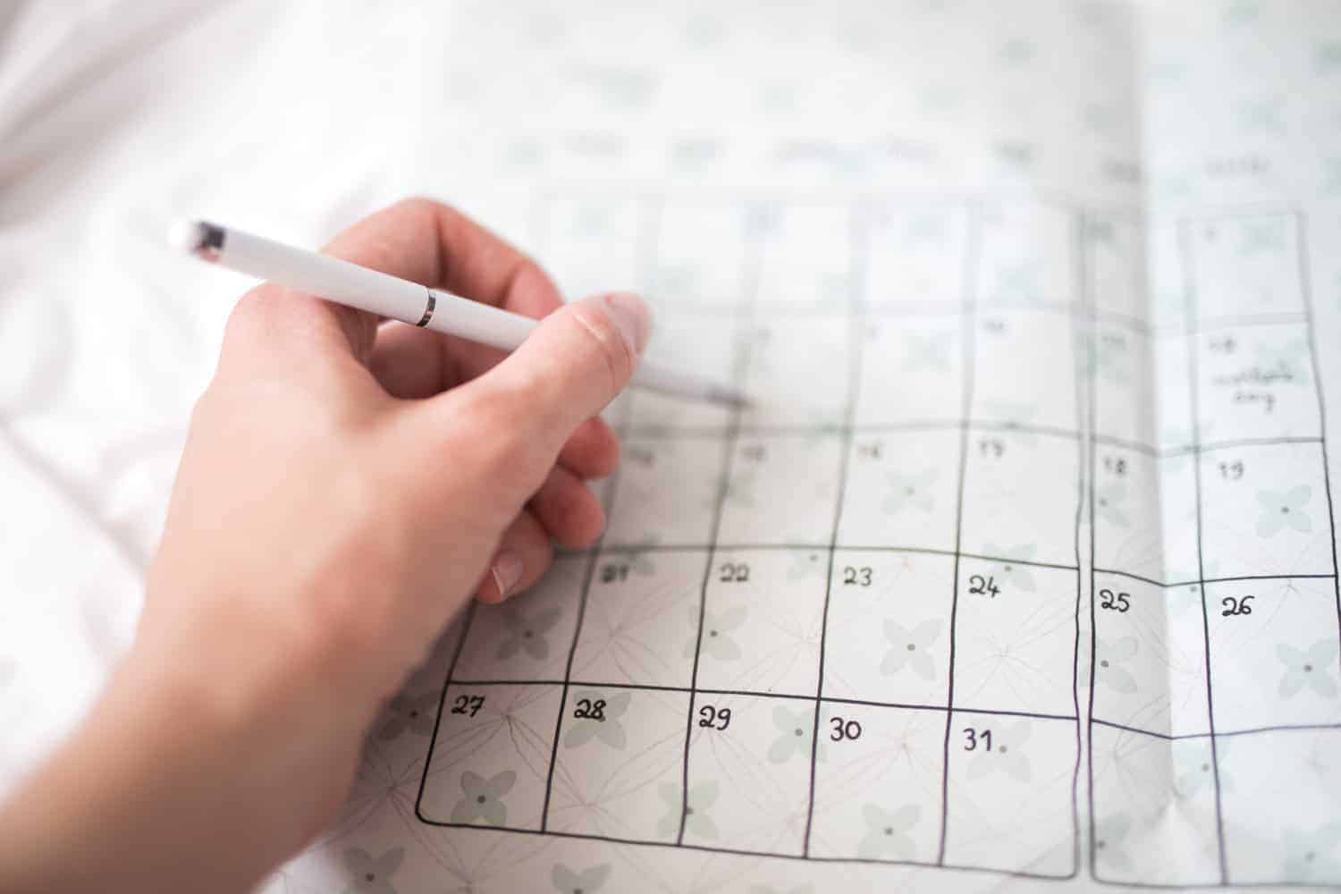 human hand with writing pen making notes on a paper calendar