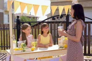 two young girls selling lemonade at a food stand to a female customer