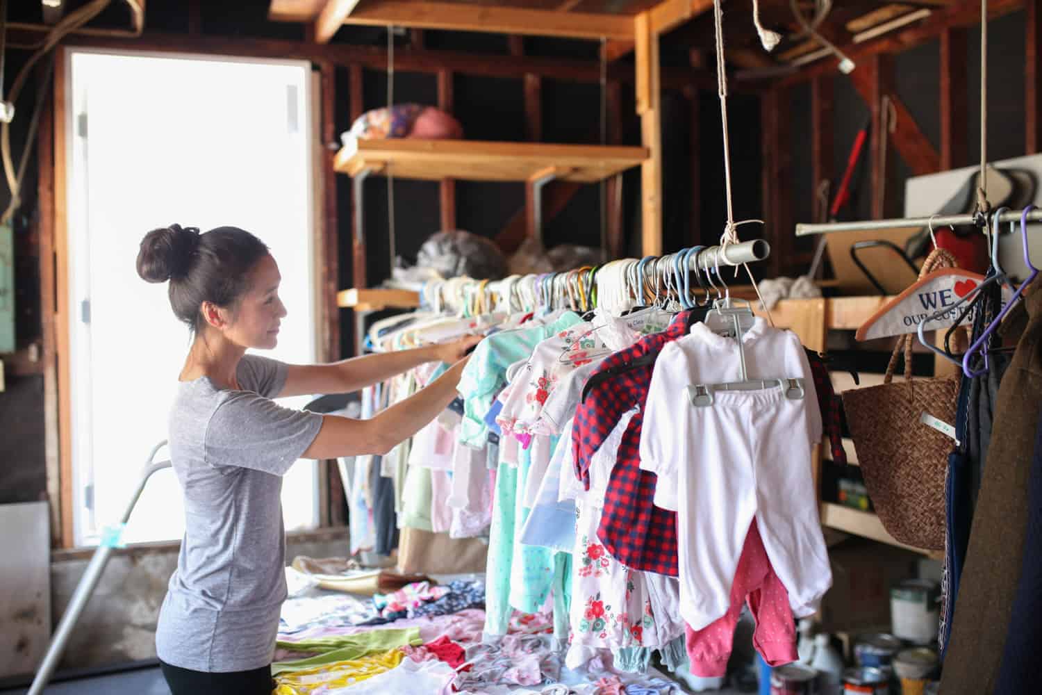 woman looking through hanging childrens clothing at a garage sale