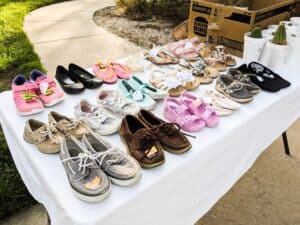 assorted childrens shoes lined up on a table during a garage sale