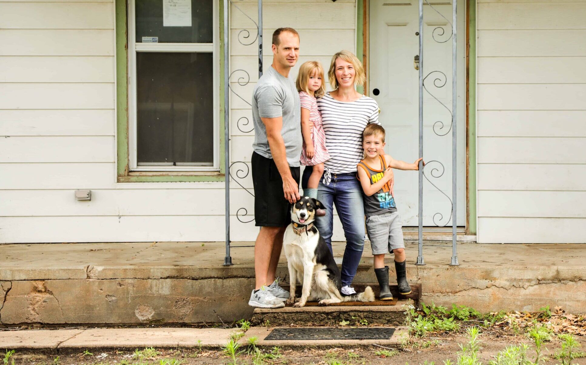 family of four and their dog posed on the front porch of their farm house