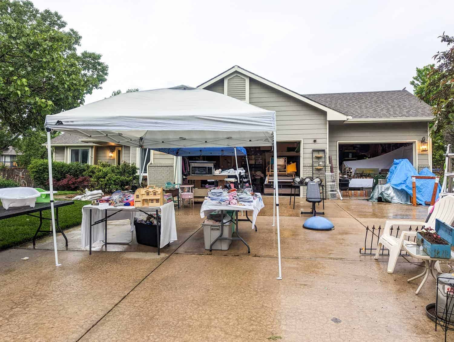 garage sale items arranged on a driveway and in a garage during a rain storm