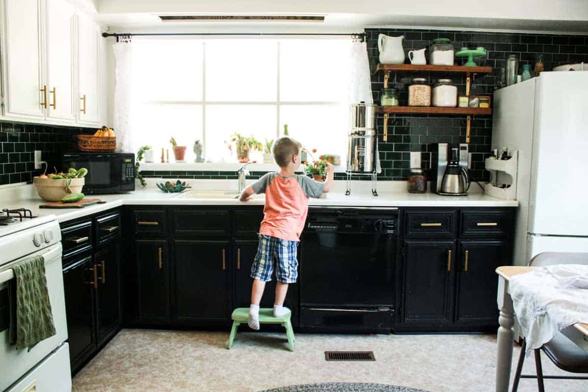 little boy stands at mobile home kitchen sink on a step stool