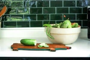 fresh cucumber and other veggies displayed on a kitchen counter with cutting board and mixing bowl